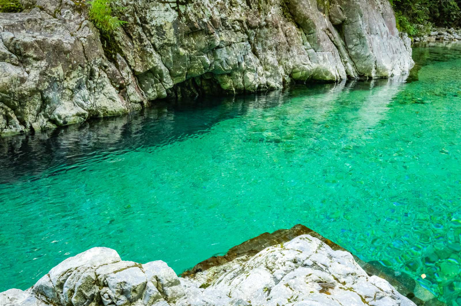 透明でエメラルドグリーンの水が流れる渓谷